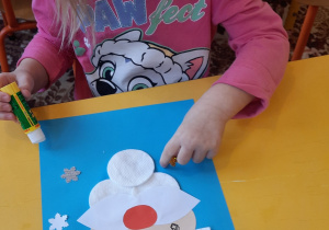 Dziewczynka przykleja śnieżynkę na kartce.
